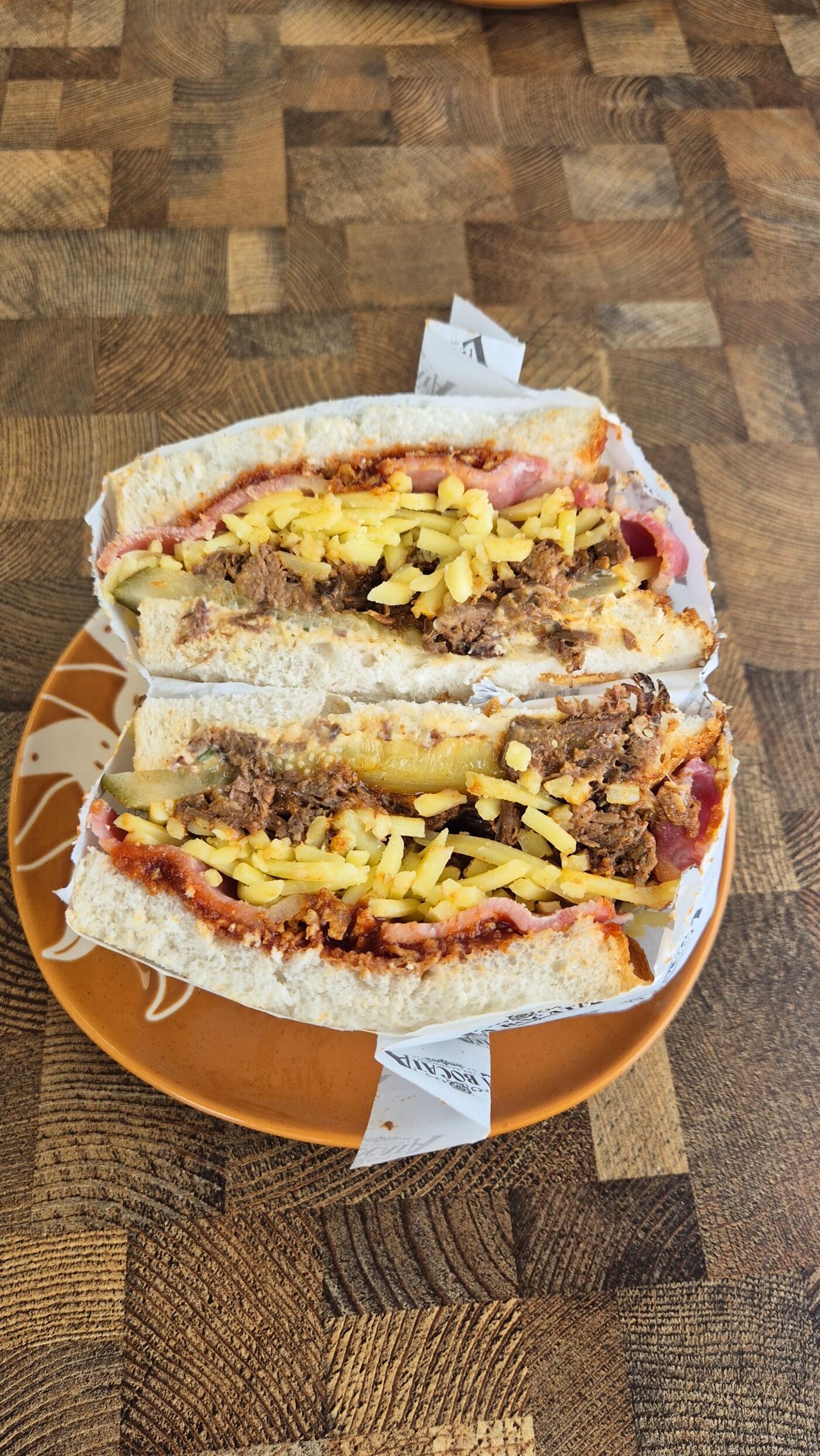 A bocata layered with slow-cooked beef, cheese and gherkins on a terracotta plate