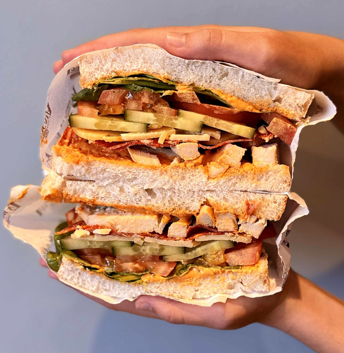 A stacked bocata held in one hand, layered with chicken, chorizo, cheese and salad
