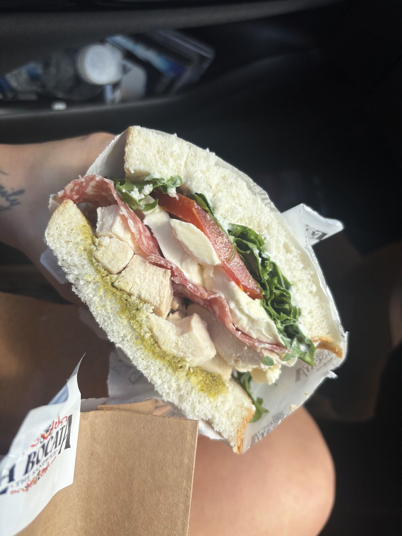 A bocata layered with pesto, chicken, salami, mozzarella and rocket, in a kraft takeaway box