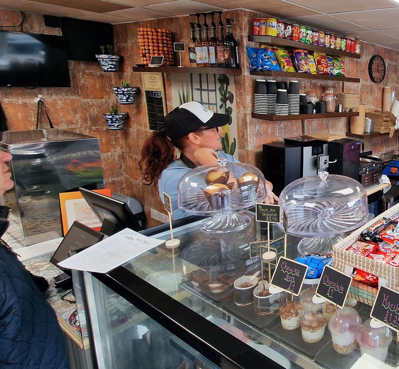 Inside La Bocata: the counter, the cake domes and the team making sandwiches to order
