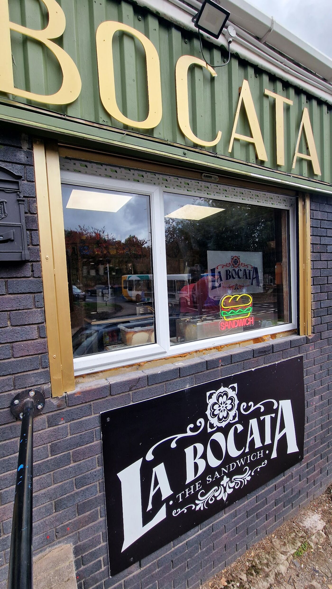 La Bocata's shopfront window on Dynevor Street, with the neon sandwich sign and tile-rosette logo plaque